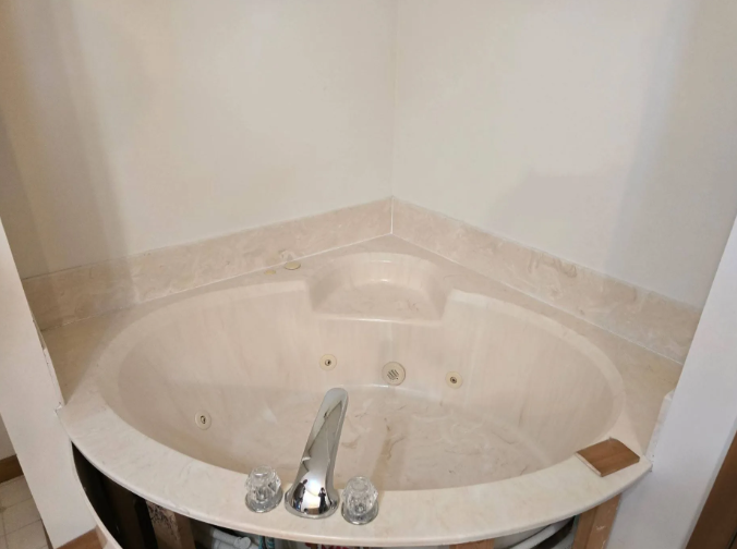 Corner jacuzzi bathtub with chrome faucet and beige tile walls