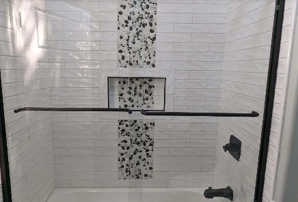 Accessible shower with white tile walls, grab bar, recessed shelf, and shower fixtures.