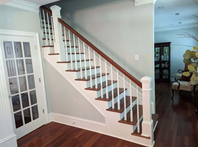 Staircase with white balusters and dark wood handrail in a bright hallway with hardwood floors