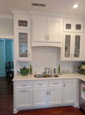 White built-in kitchen cabinets with glass doors, mosaic backsplash, and countertop decor in a bright room