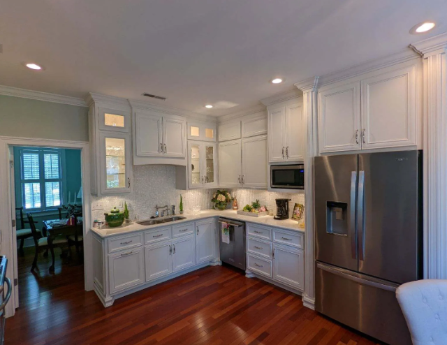 Bright white modern kitchen with stainless steel refrigerator, hardwood floors, and corner cabinets