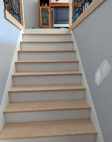 Indoor staircase with light wooden steps, white risers, and gray walls leading to an upper floor