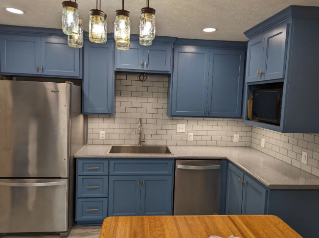 Blue kitchen with stainless steel appliances, white subway tile backsplash, and pendant lights over a wooden table