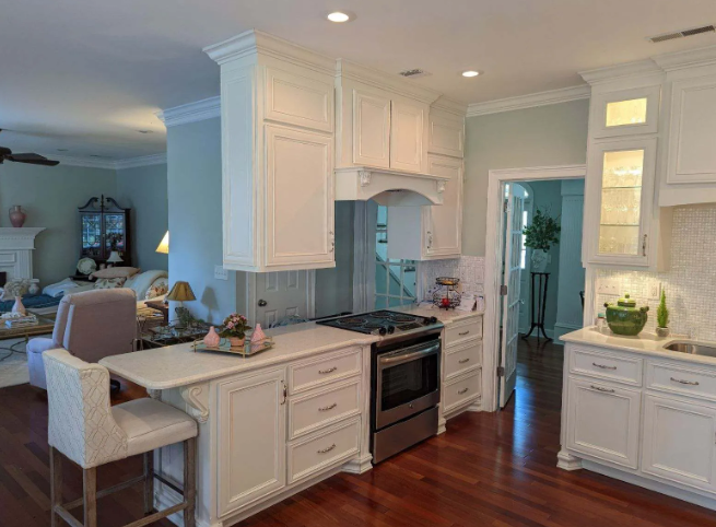 Bright white kitchen with island, wood floors, and adjacent living area in the background