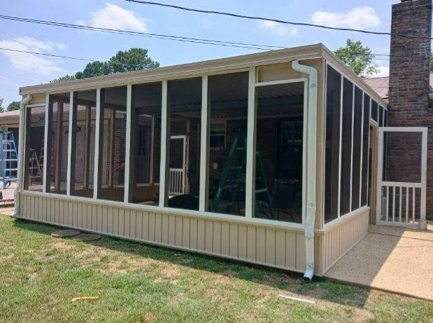 Screened porch addition with beige siding, large windows, and a brick chimney beside it