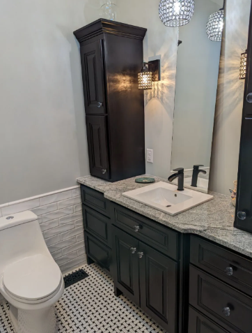 Compact bathroom with white toilet, dark vanity, granite counter, and mirror under wall sconces.