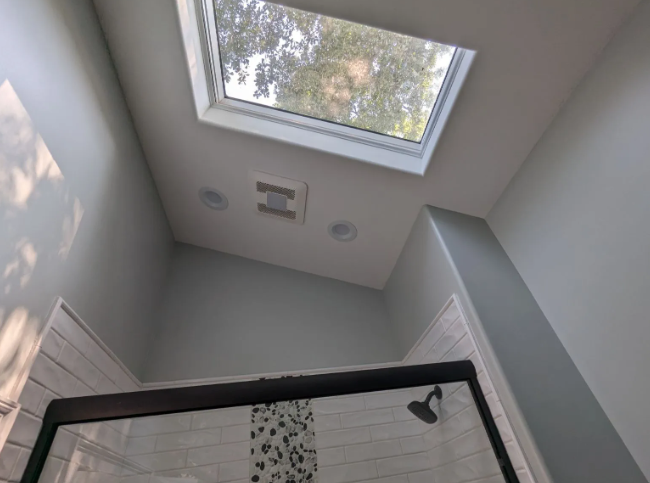 Looking up at a skylight in a gray shower with tiled walls and a black showerhead.