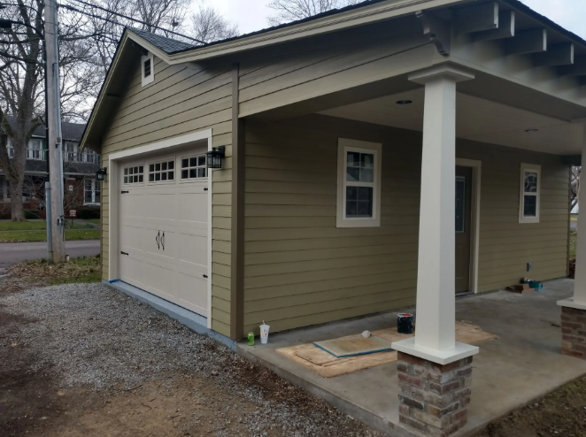 Detached beige garage with white door and front porch columns in a residential yard