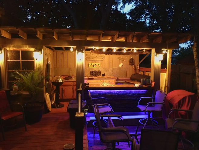 Warmly lit backyard patio with bar seating, blue accent lights, and a pergola at night