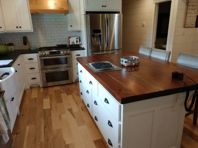 Bright kitchen with a large wooden island, stainless stove, white cabinets, and hardwood floors.