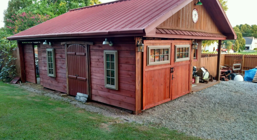 Red wooden barn-style outbuilding with a metal roof, doors, windows, and gravel driveway