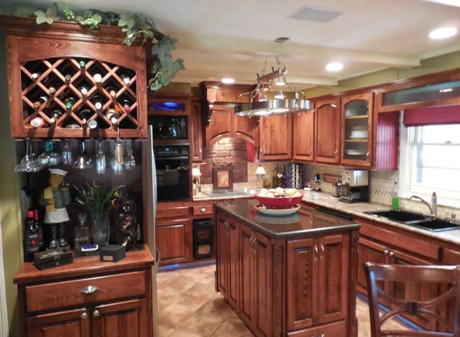 Warm kitchen with wooden cabinets, granite island, wine rack, and hanging glassware.