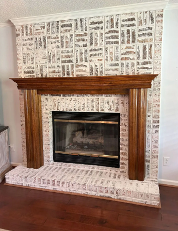 Wood-paneled fireplace with a wood mantel and newspaper-print wallpaper surround in a room with hardwood floors