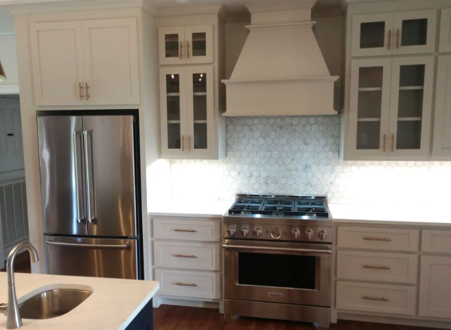 Modern white kitchen with stainless steel refrigerator, stove, cabinets, and granite island sink