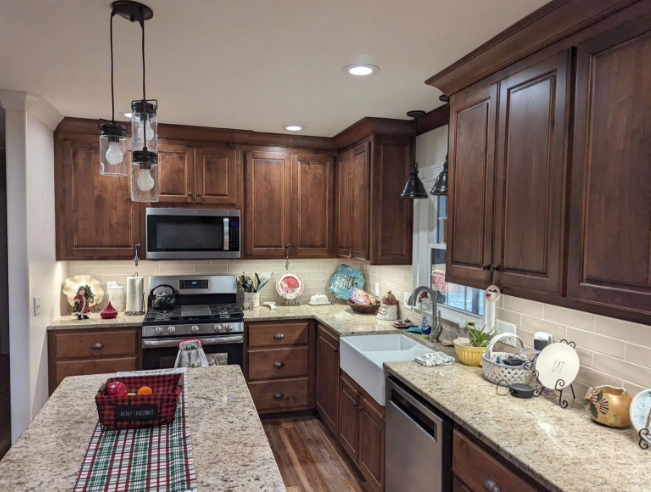 Warm kitchen with dark wood cabinets, granite island, and stainless steel appliances.