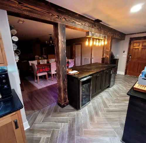 Rustic kitchen with dark wood island, herringbone floor, exposed beams, and dining area beyond