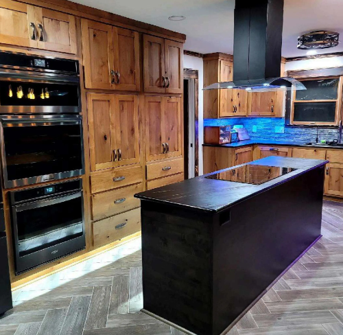 Modern kitchen with dark island, wood cabinets, built-in ovens, and blue under-cabinet lighting