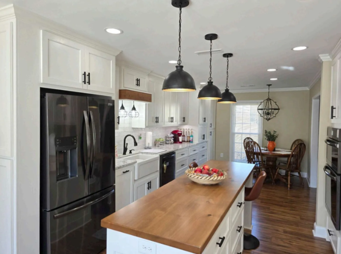Modern white kitchen with black pendant lights, wood island, and dining area in the background