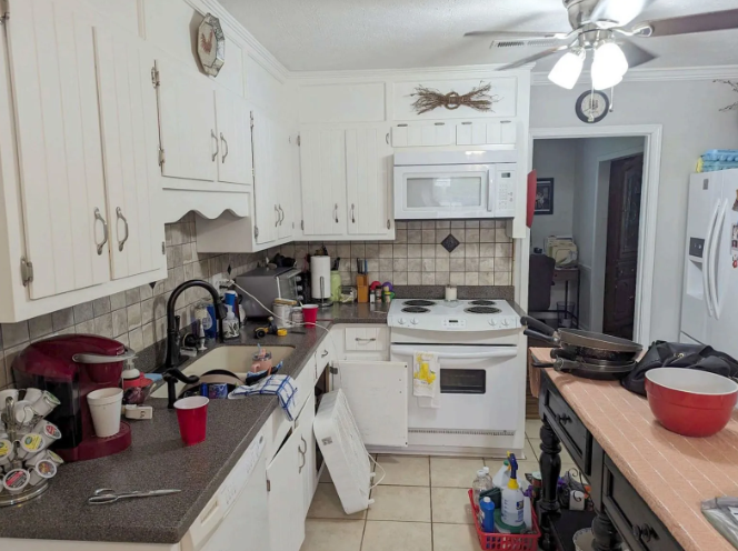 Cluttered white kitchen with dishes, utensils, and cookware on counters and a wooden island.