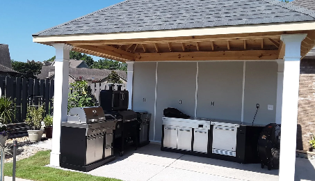 Covered backyard patio with grill, storage cabinets, and a row of white trash bins under a wooden roof.