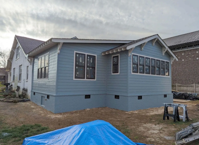Blue house under renovation with unfinished yard and overcast sky