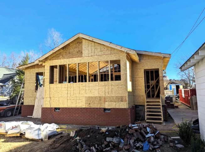 Partially renovated house with exposed framing, yellow siding, and a pile of debris in front