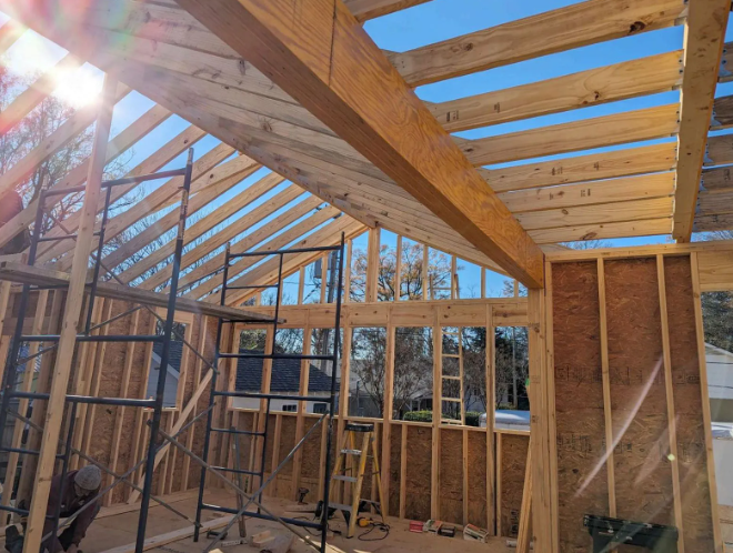 Sunlit unfinished wooden interior with exposed rafters, framing studs, and skylight panels
