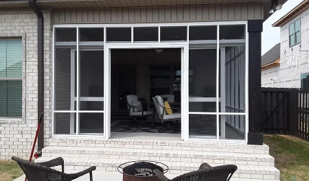 Patio with screened porch and sliding glass doors, overlooking two white lawn chairs outside.