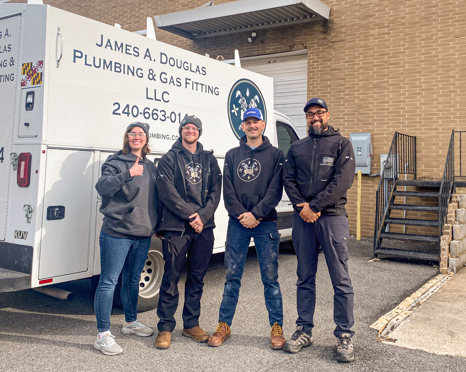 Four people stand in front of a plumbing truck. The truck has the company name James A. Douglas Plumbing. One gives a thumbs-up.