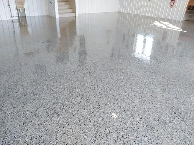 A shiny concrete floor in a garage with a staircase in the background.