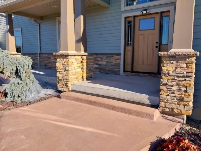 The front porch of a house with a wooden door and stone pillars.