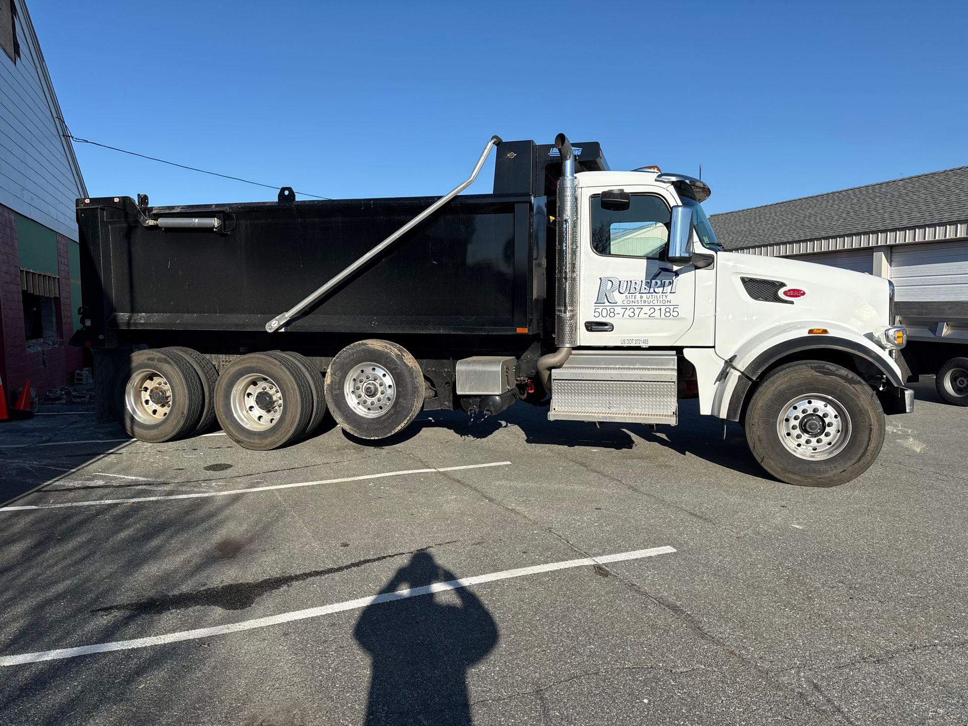 White dump truck parked on asphalt, shadow of person visible.