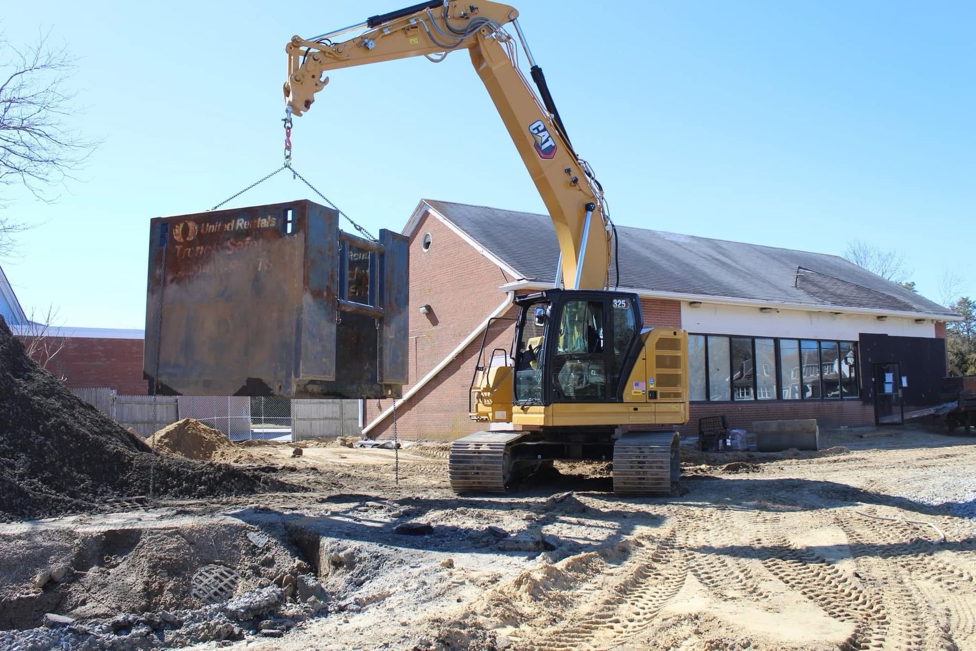 Excavator lifting a large concrete section of a building during demolition in an outdoor setting.