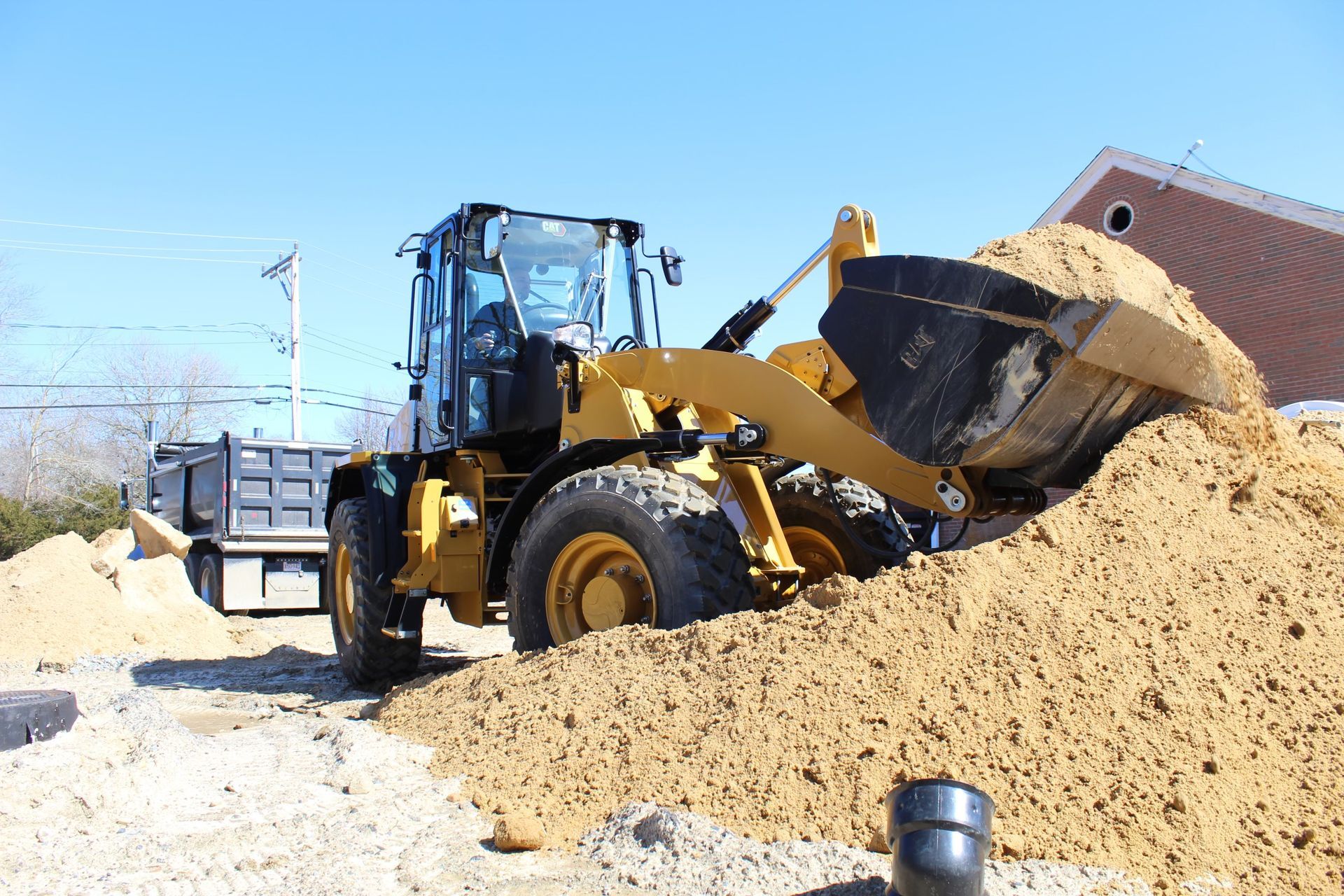 Yellow loader scoops sand, near a truck, on a sunny day.