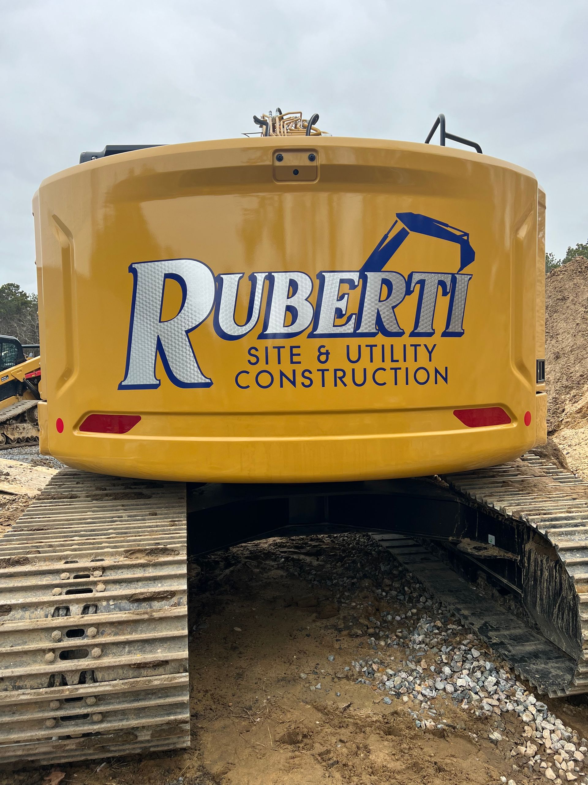 Yellow Ruberti construction excavator with logo on rear, tracks on ground.