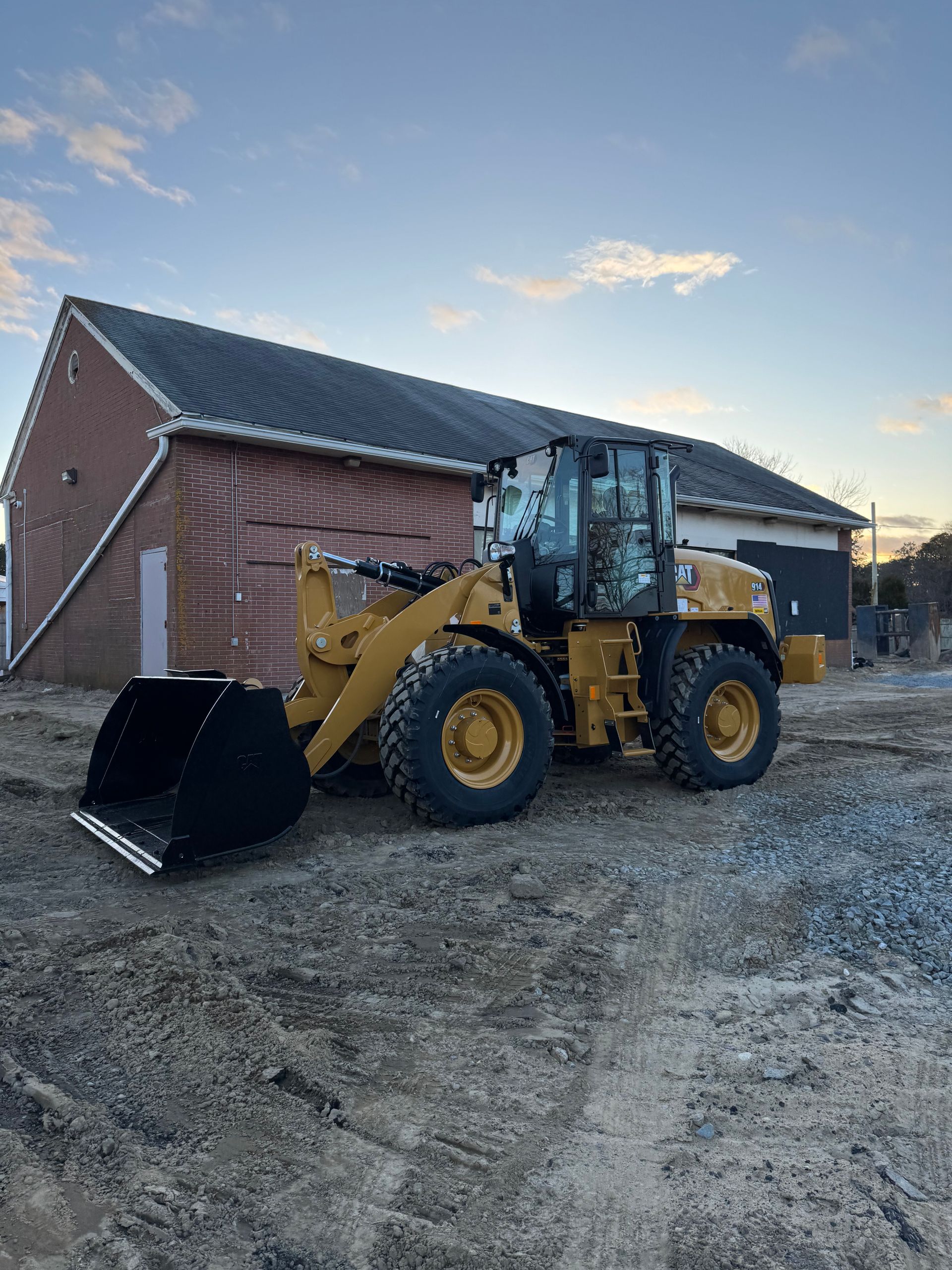 Yellow Caterpillar loader parked near a brick building.