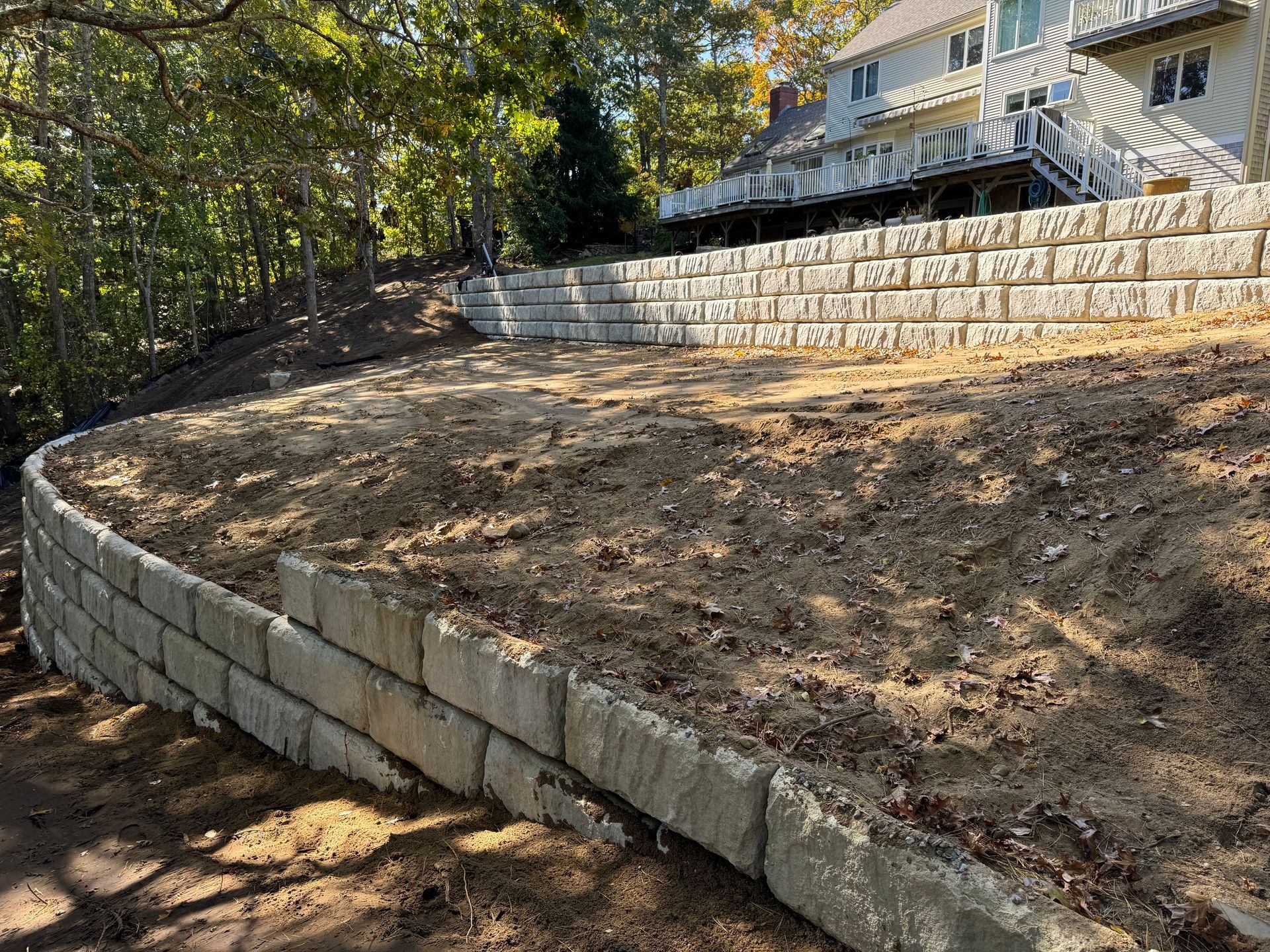 Retaining walls of stacked concrete blocks on sloped land, with a house in the background.