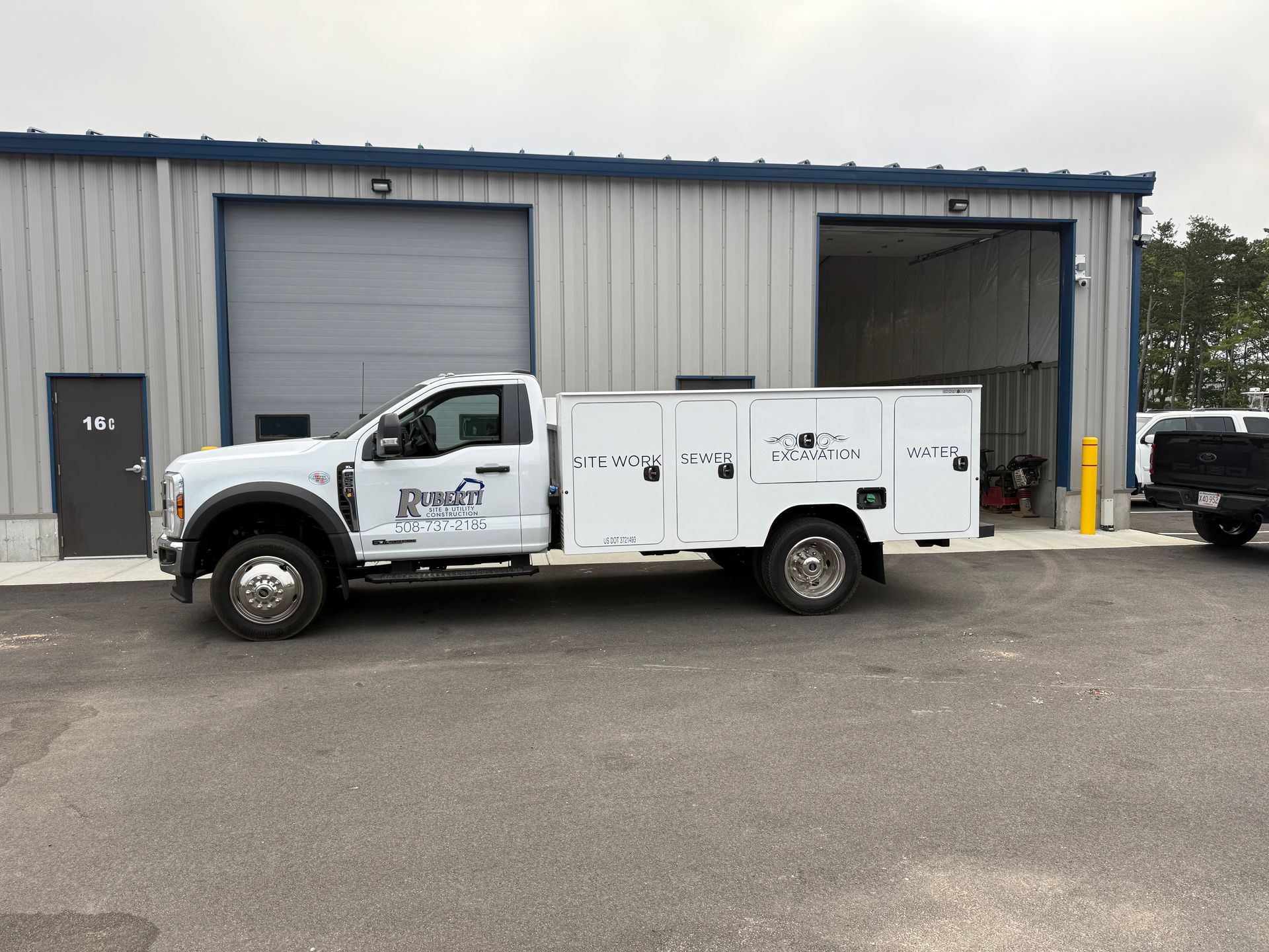 White work truck parked in front of a gray metal building with garage doors.