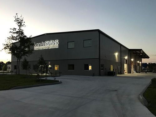 Modern gray office building at dusk with lit windows and a driveway