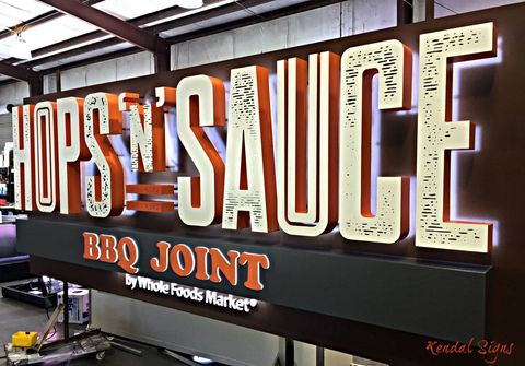 Large “Hops ’n Sauce” BBQ Joint sign with orange and cream lettering on a dark wall.