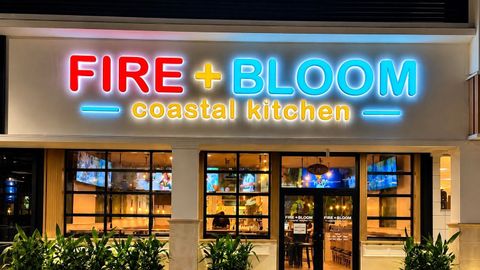 Neon-lit Fire + Bloom Coastal Kitchen storefront at night with warm interior lights and potted plants
