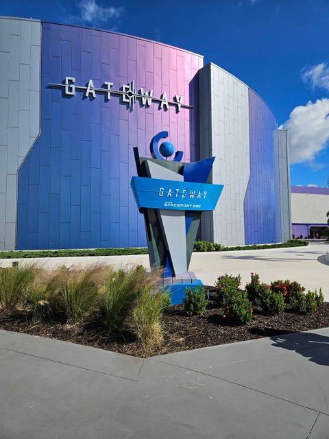 Entrance sign outside a colorful purple building with a blue sky and landscaping in front