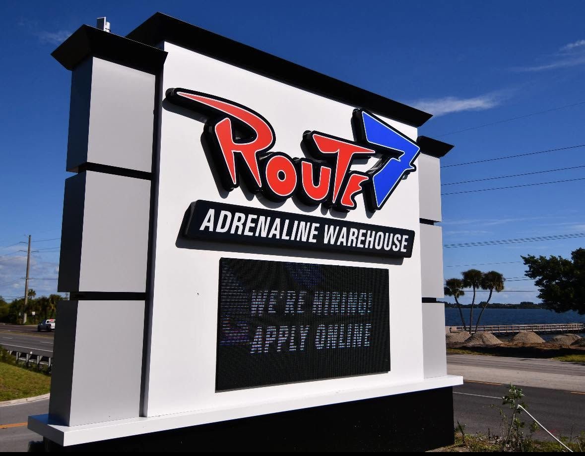 Route 66 Adventure Warehouse roadside sign under a blue sky with bold red, black, and white lettering
