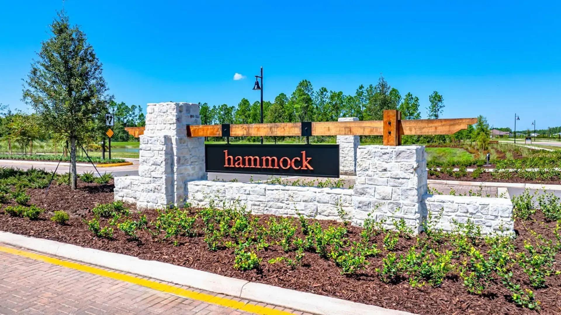 Stone entrance sign reading “hammock” beside a landscaped roadside with shrubs and young trees