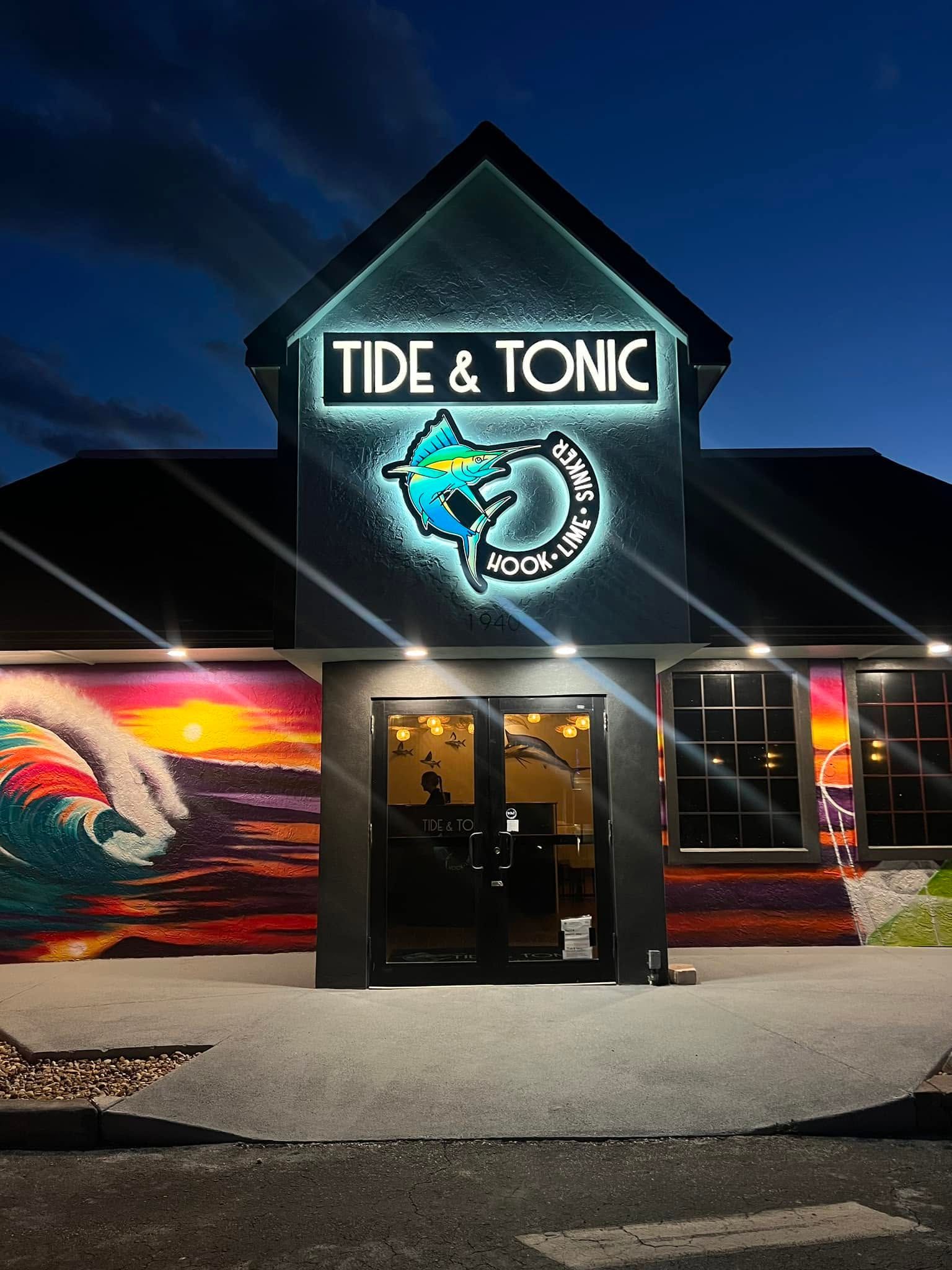 Tide & Tonic storefront at night with neon sign and colorful wave murals