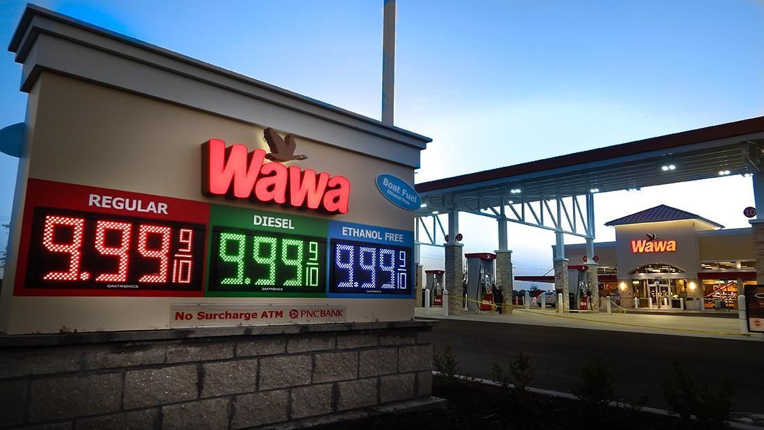 Wawa convenience store at dusk with bright red, green, and blue gas price signs outside