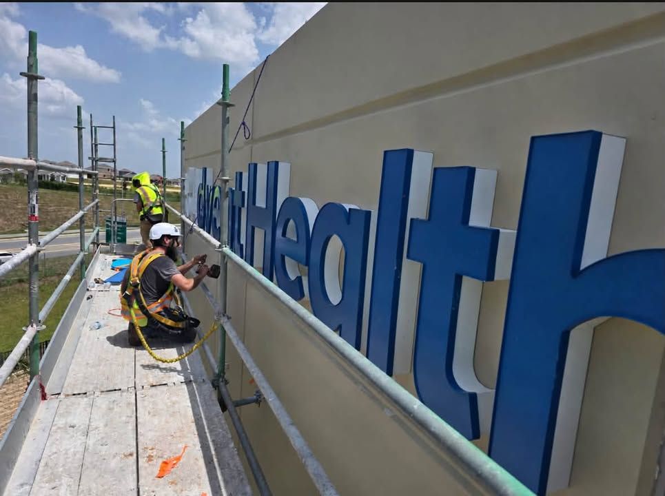 Workers installing blue signage on a building wall outdoors
