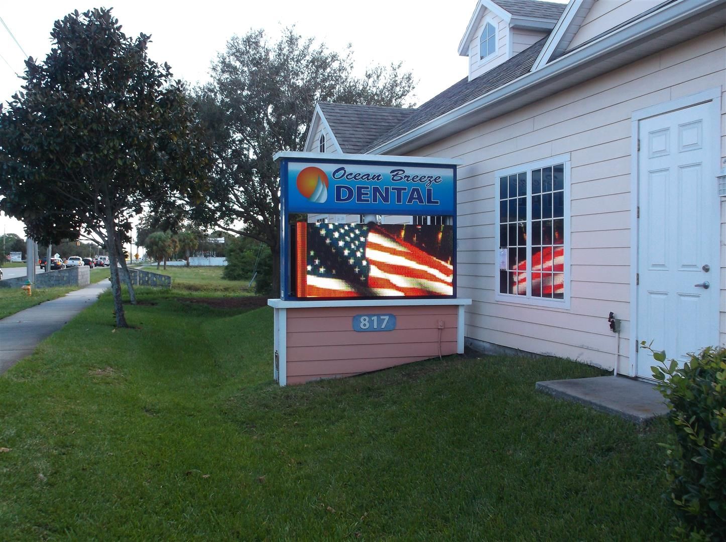 Dentist office sign beside a white building and grassy lawn at dusk