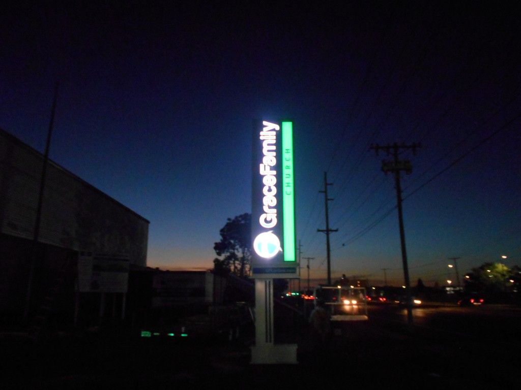Illuminated Cricket Wireless roadside sign at dusk with cars and utility poles nearby