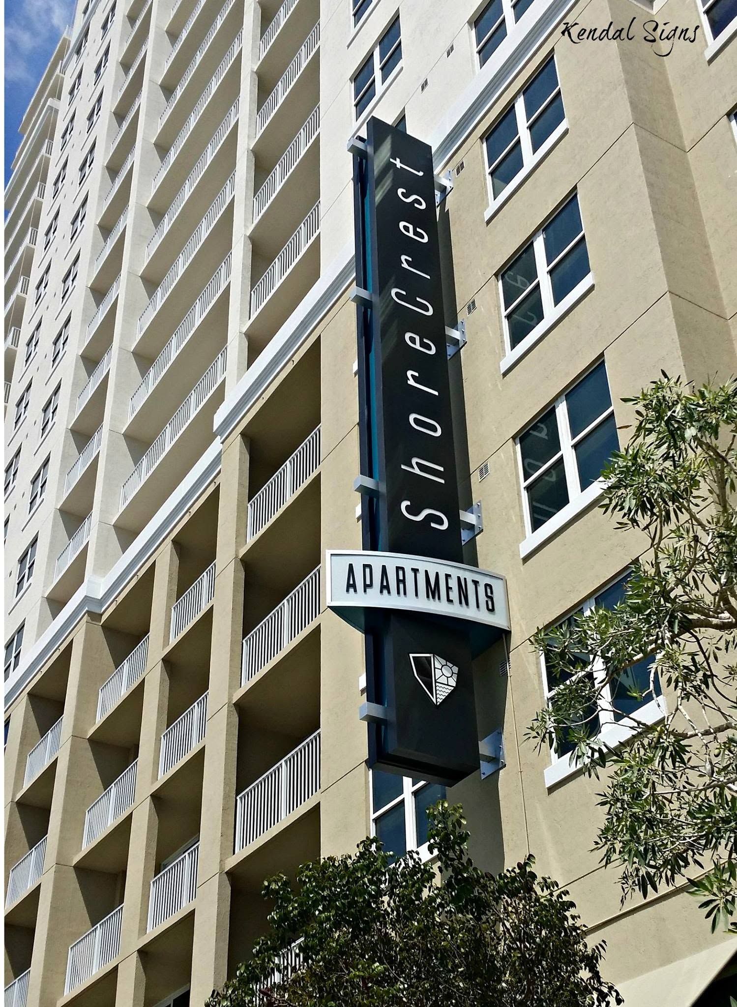 Vertical neon sign on a beige high-rise building with balconies and windows.